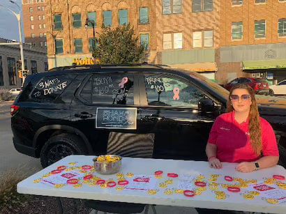 Woman at a table with breast cancer awareness materials in front of a car.