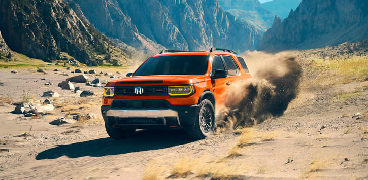 An orange 2026 Passport driving across the sandy grassland, with dust and sand billowing from its tires.