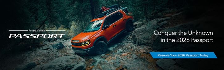 An orange 2026 Honda Passport navigates rocky terrain in a wooded landscape, promoting adventure and exploration. Reserve yours today!