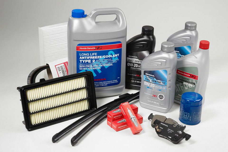A collection of Honda car maintenance products, including antifreeze, motor oil, a blue oil filter, air filters, spark plugs, and windshield wipers.