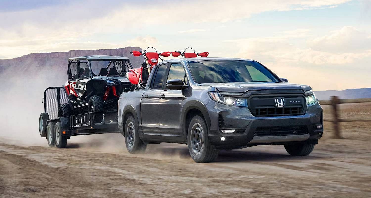 The 2025 Honda Ridgeline TrailSport in Modern Steel Metallic drives through a dirt field towing a trailer