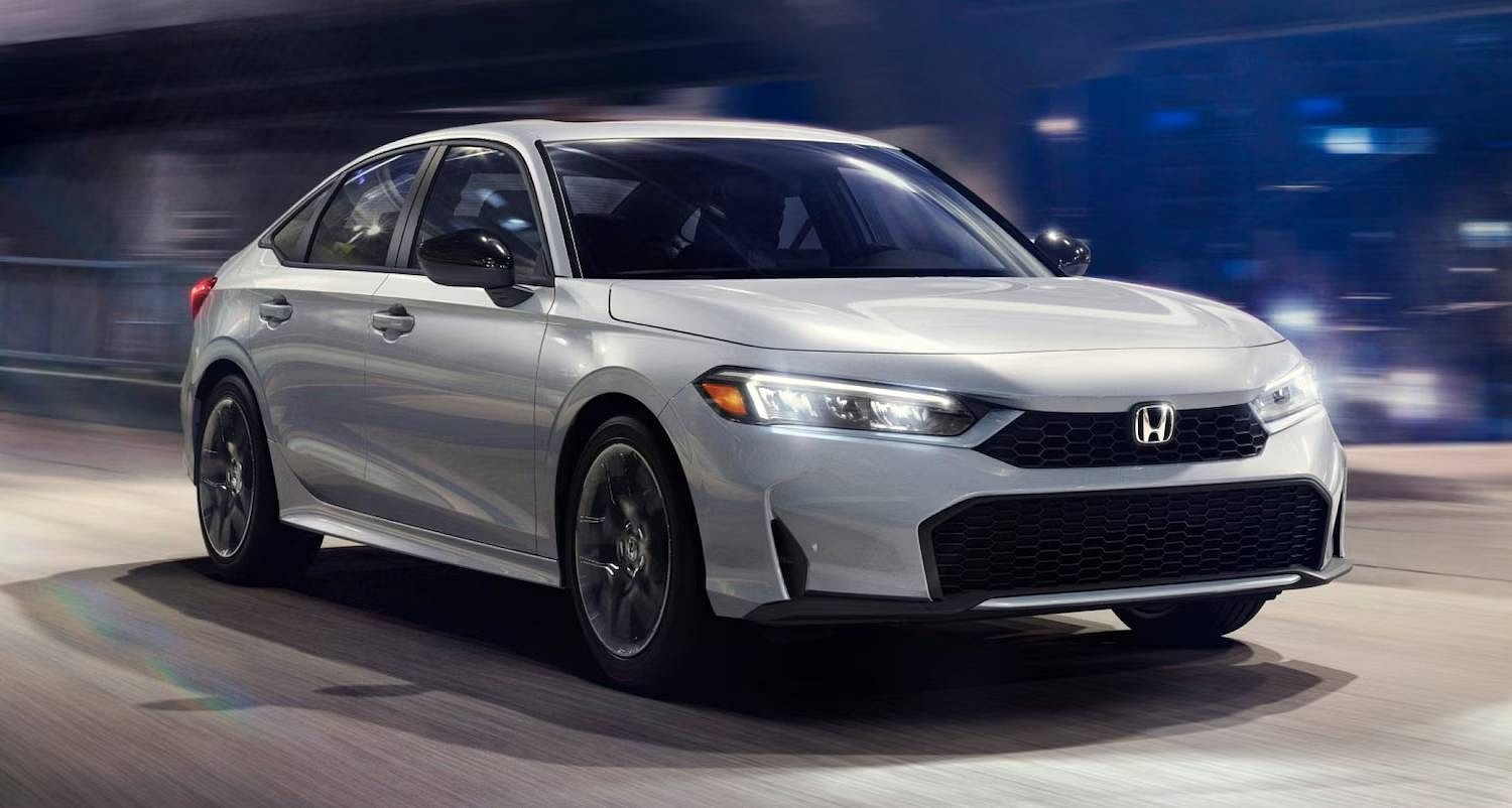 The 2025 Honda Civic Sedan LX in Solar Silver Metallic driving at night, with urban bridge and the city behind