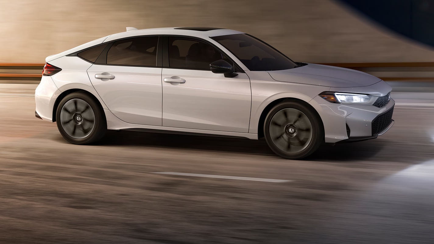 A 2026 Honda Civic Hatchback Hybrid with a modern design drives swiftly on a blurred urban road, conveying a sense of speed and sophistication.
