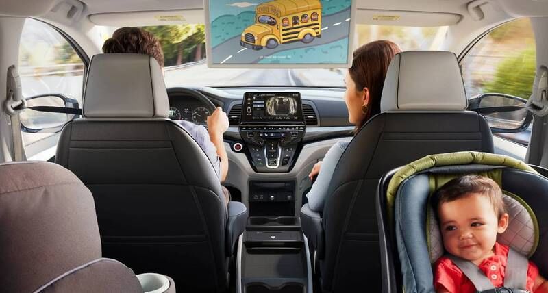 The 2026 Honda Odyssey Elite with man driving and woman in front passenger seat, driving on residential road