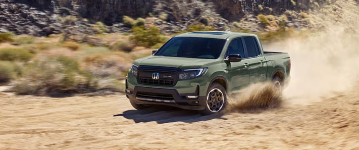 2026 Ridgeline TrailSport in Ash Green Metallic driving through rugged terrain with dust kicking up, with mountains in background, at sunrise.