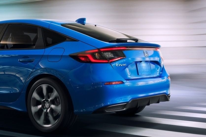 A sleek blue 2025 Honda Civic Hatchback captured from the rear, showcasing its modern design and dynamic lines against a blurred background.