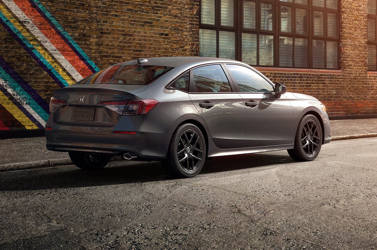 Sleek gray 2026 Honda Civic Sedan parked on a street beside a brick wall with colorful diagonal stripes and windows, conveying a modern and urban ambiance.