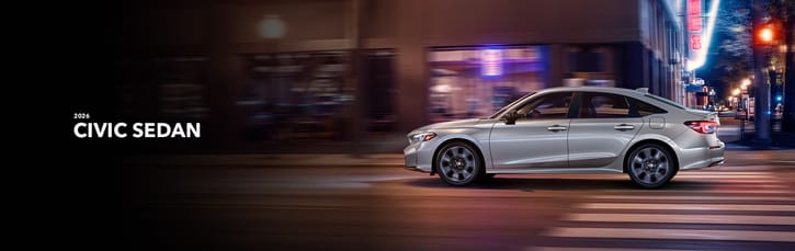 A silver 2026 Honda Civic Sedan driving through an urban street at night, with blurred city lights in the background conveying motion and modernity.