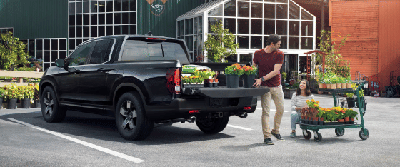 2026 honda Ridgeline RTL in Crystal Black Pearl, people loading truck bed with garden supplies in front of home improvement store.