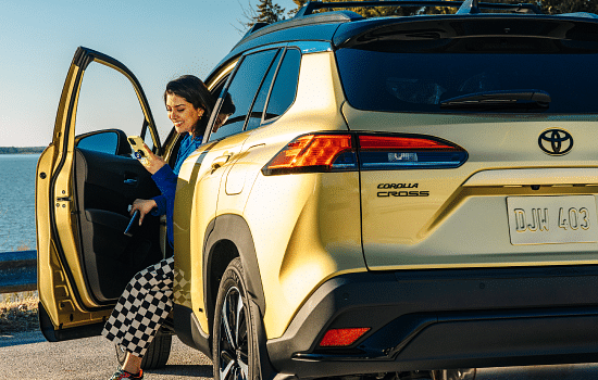 Woman next to a lake looking at her phone smiling sitting in a Toyota Corolla Cross