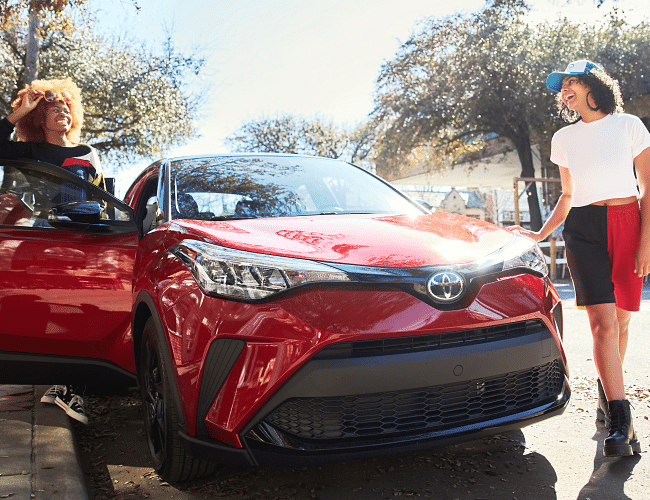 Two women standing and smiling next a Toyota C-HR