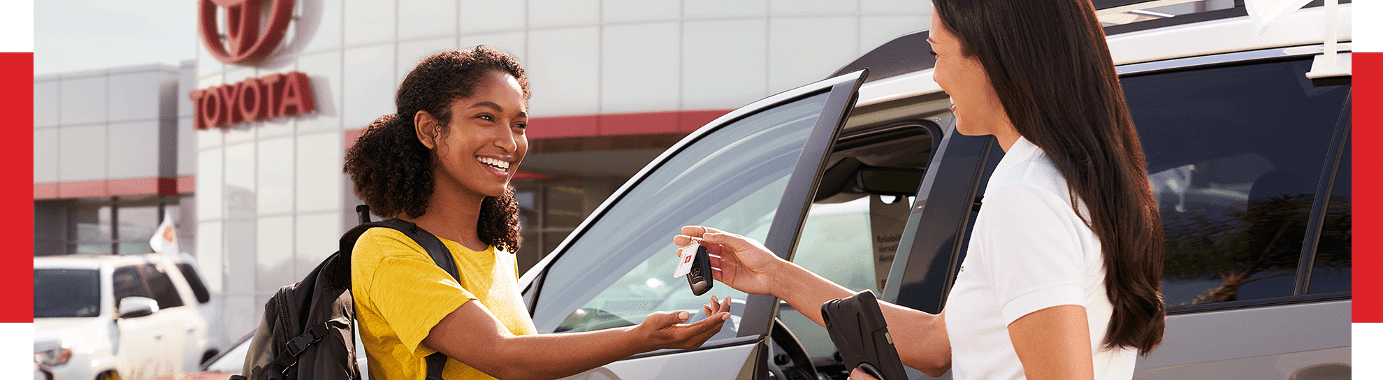 A woman handing car keys to another woman in front of a Toyota dealership
