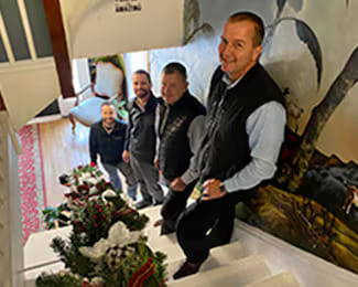 Four men posing on an indoor staircase decorated with Christmas garland.