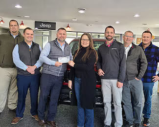 Group of Tri City Cars employees presenting a check donation to a woman inside the Jeep dealership showroom.