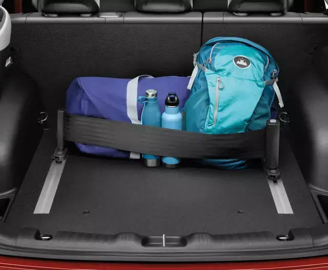 A car trunk containing a teal backpack, a blue duffel bag, and two reusable water bottles secured in place by a horizontal strap to prevent movement during transit.
