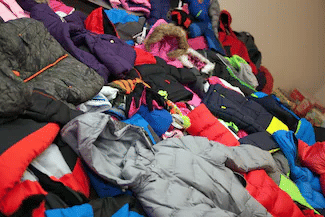 Large, overflowing pile of donated winter coats, jackets, and hats of various colors and sizes.