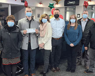 Group of Tri City Cars employees presenting a check donation inside the Jeep dealership showroom, decorated with balloons.