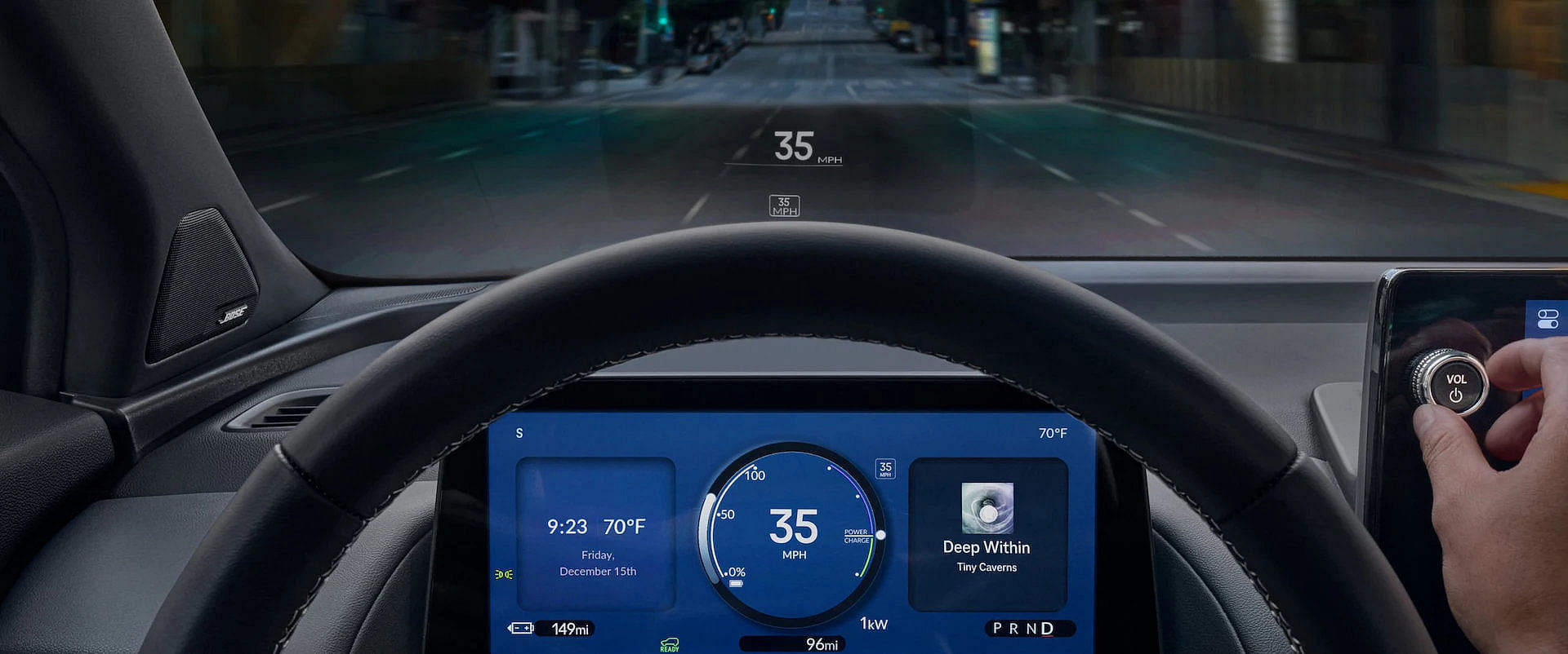 Driver's perspective inside the 2025 Honda Prologue, showing the digital instrument cluster, center infotainment screen, and head-up display projecting speed onto the windshield while driving on a city street at night. A hand adjusts the volume knob.