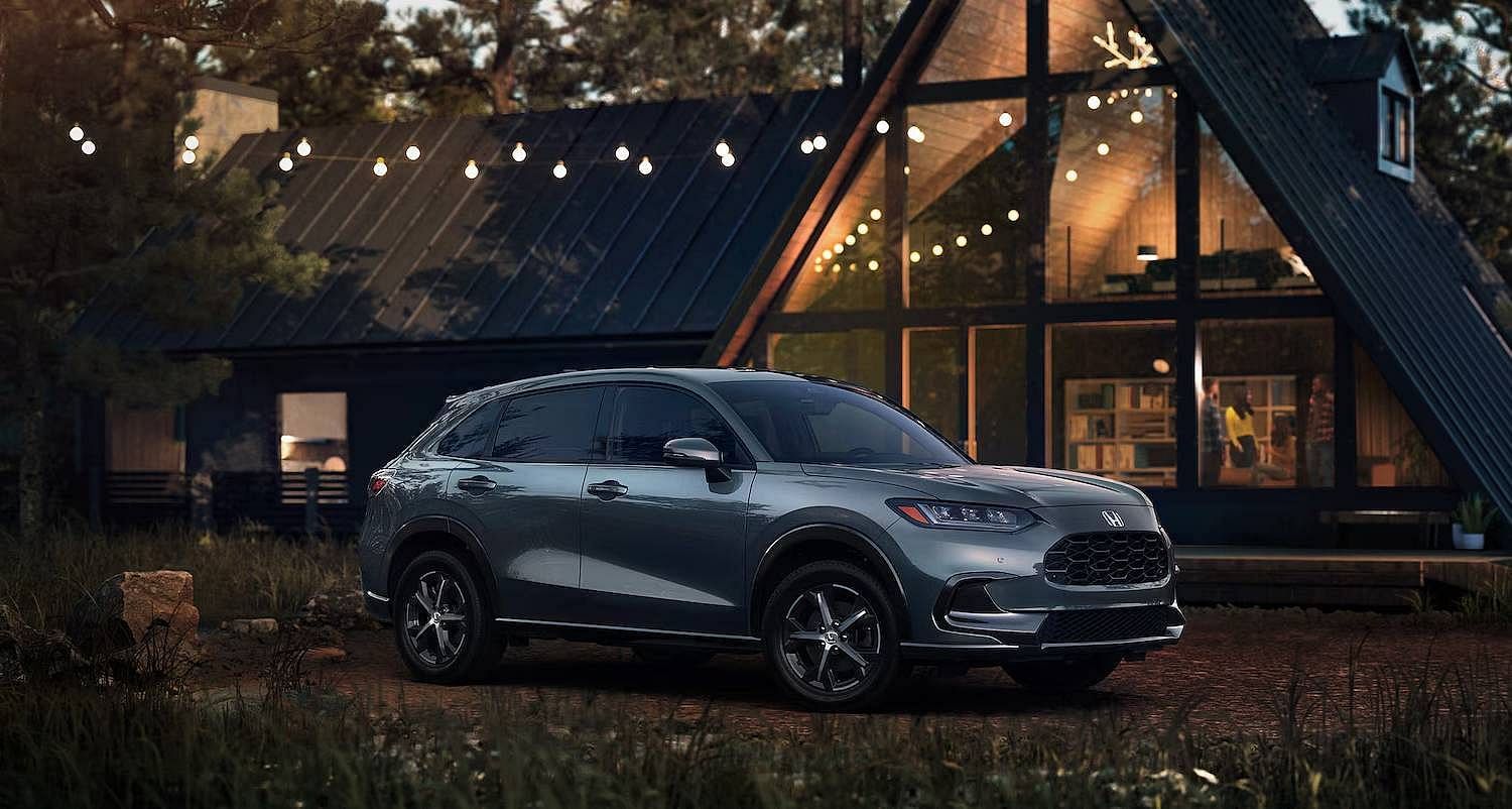 Passenger-side view of the 2026 Honda HR-V EX-L in Nordic Forest Pearl shown parked beside an A-frame cabin at dusk