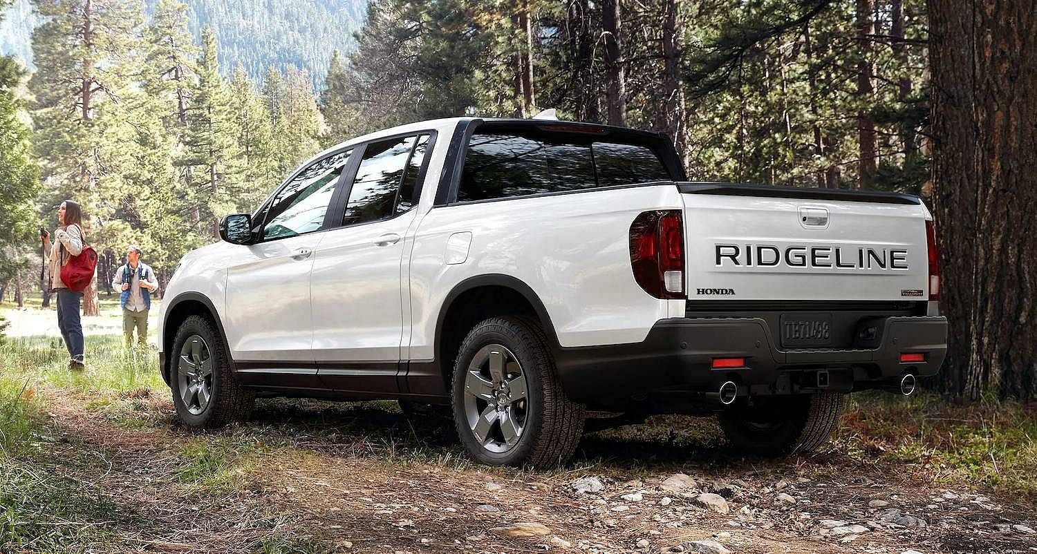 The 2025 Honda Ridgeline TrailSport in Platinum White Pearl parked next to two hikers in the mountains between tall trees