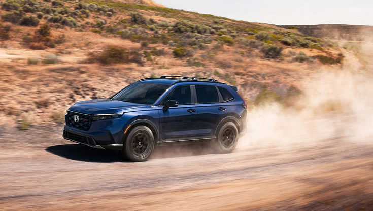 A blue Honda CR-V driving on a dirt road, kicking up a cloud of dust.