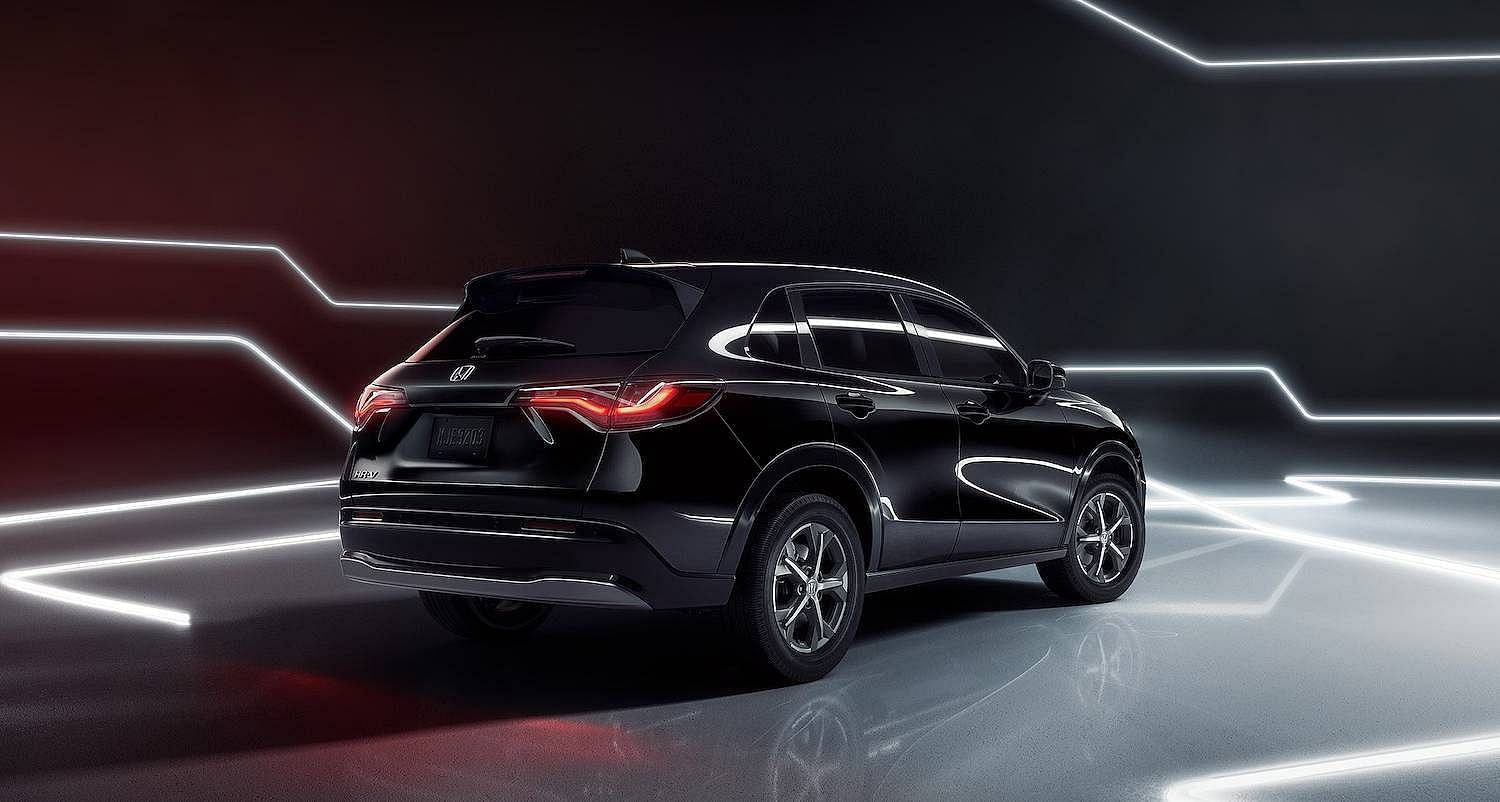 Rear passenger-side view of the 2026 Honda HR-V EX-L in Crystal Black Pearl shown parked on a reflective surface and surrounded by neon lights
