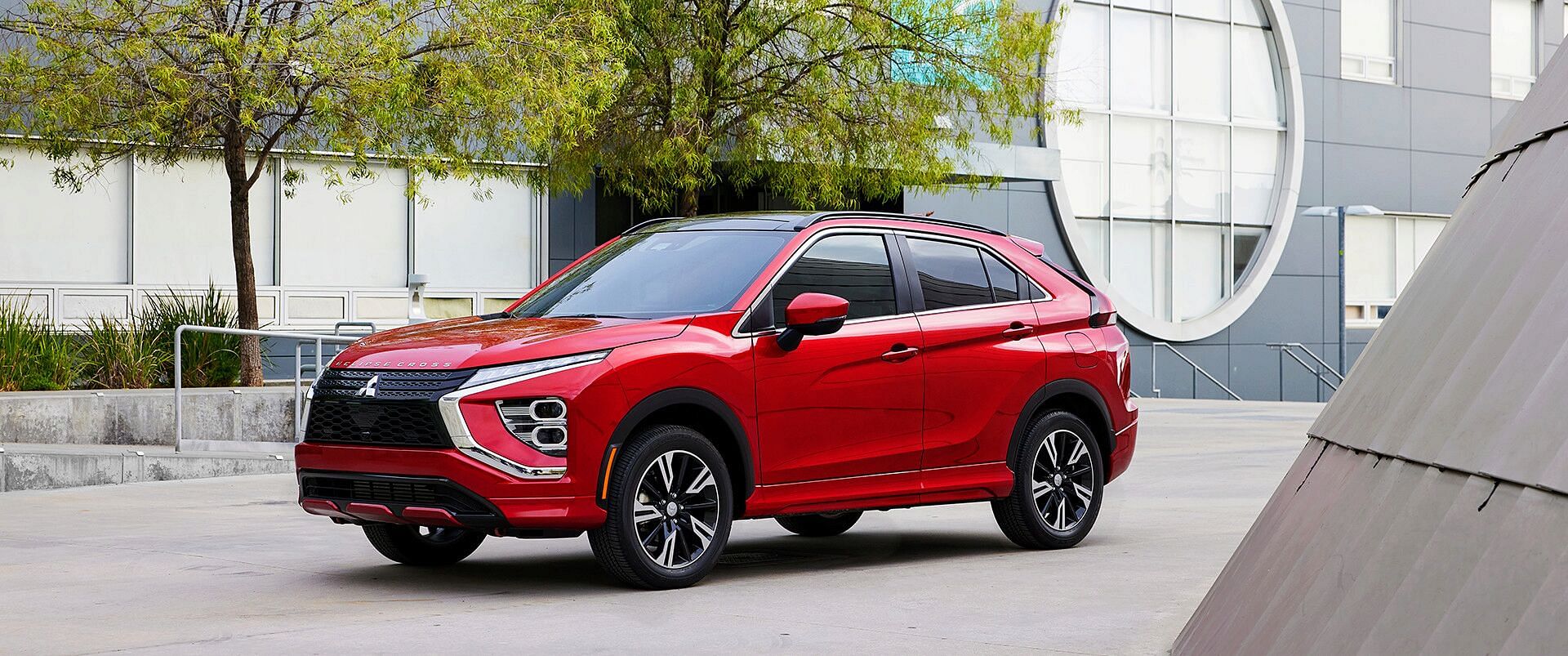 A red 2023 Mitsubishi Eclipse Cross stands on the street. Gray building in the background