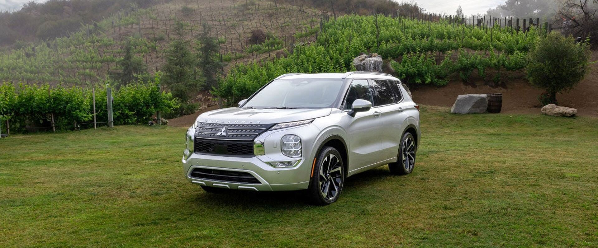 A silver 2023 mitsubishi outlander standing in a clearing. Hills in the background