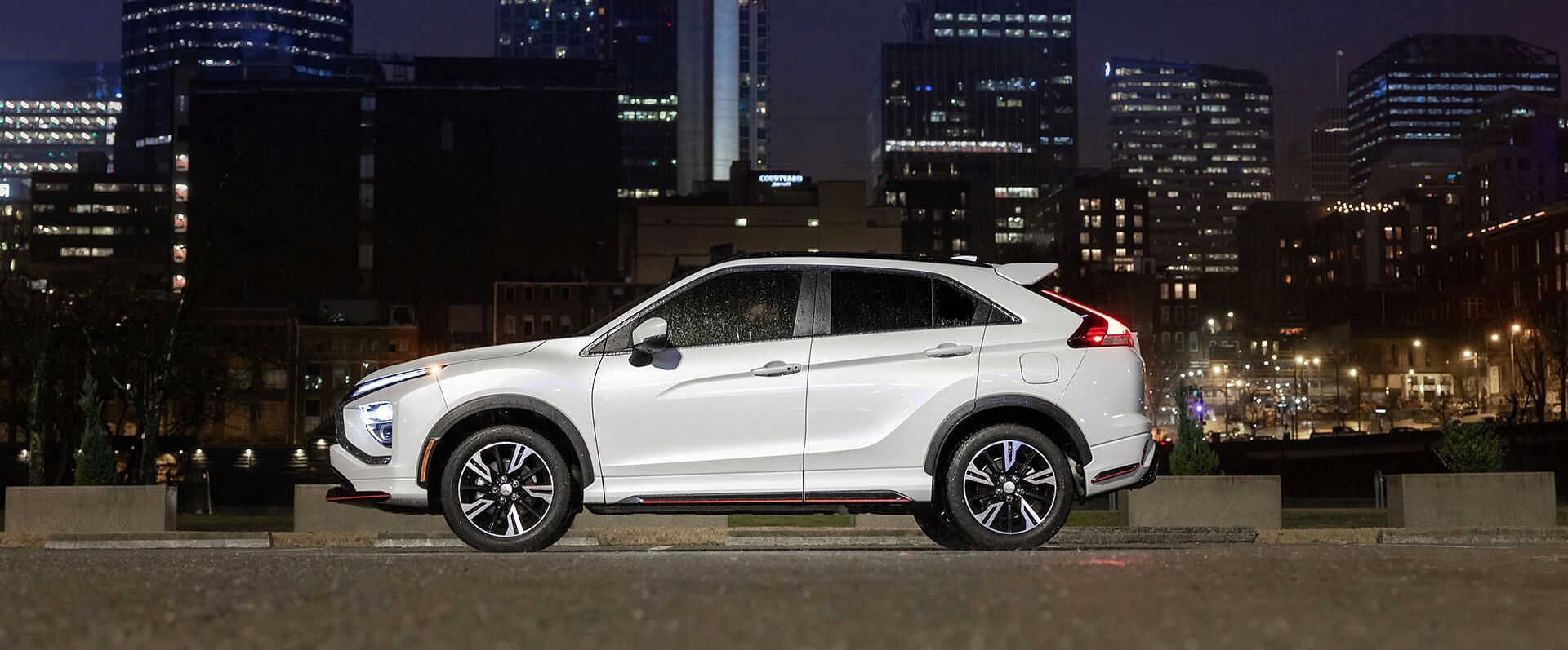 A white 2023 Mitsubishi Eclipsce Cross standing in a parking. In the background, the city at night.