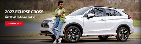 A woman in a green shirt and jeans stands leaning against a white 2023 Mitsubishi Eclipse Cross