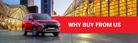 WHY BUY FROM US white text on red background and a red Mitsubishi SUV parked between modern building