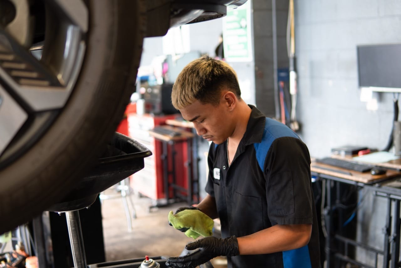 A techincian repairs a car in a garage, surrounded by tools and equipment, focused on his work.