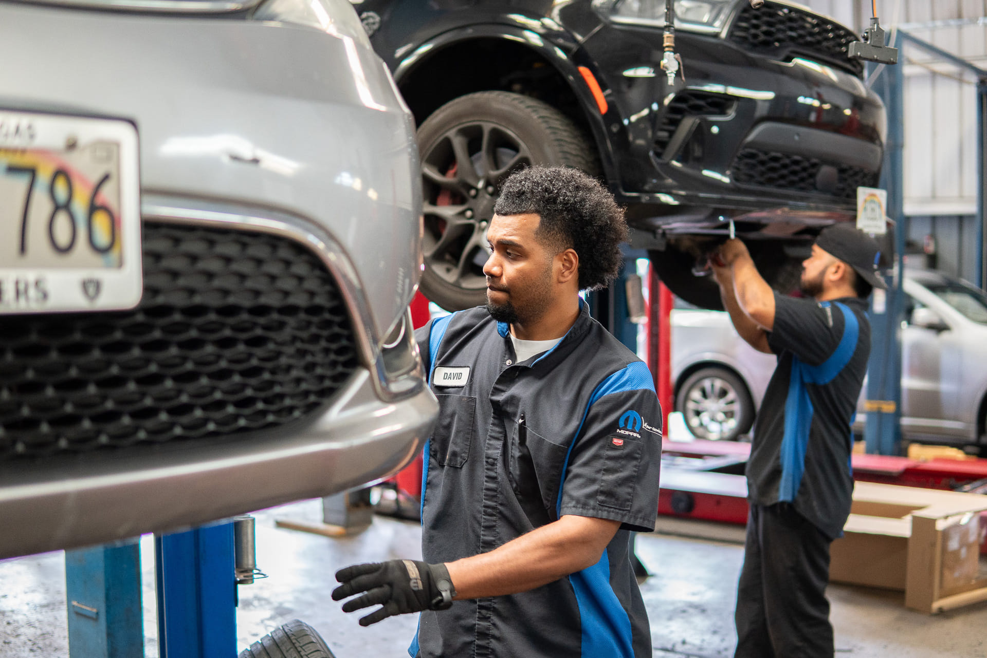 Two technicians repairing a car in a garage, surrounded by tools and equipment, focused on their work.