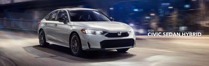 White 2026 Honda Civic Sedan Hybrid driving through an urban nightscape. The blurred city lights create a dynamic and sleek atmosphere, highlighting its modern design.