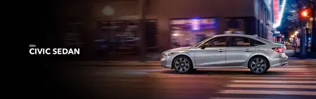 A silver 2026 Honda Civic Sedan driving through an urban street at night, with blurred city lights in the background conveying motion and modernity.