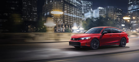 A red Civic driving through a city at night.