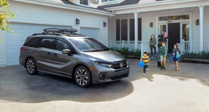 The 2026 Honda Odyssey Elite in Modern Steel Metallic with accessories parked in front of a house with family walking to the vehicle